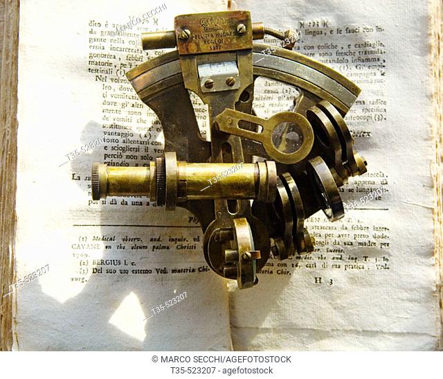 A nautical sextant resting on top of an antique book printed in Italy in 17th century