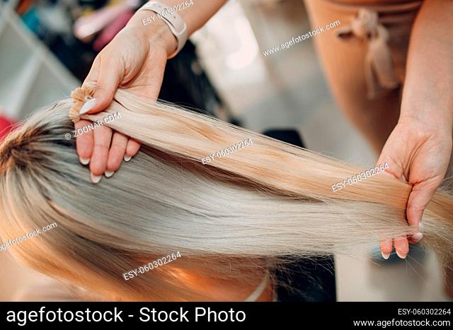 Hairdresser female making hair extensions to young woman with blonde hair in beauty salon. Professional hair extension strand of hair