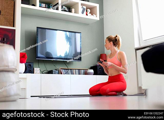 Attractive sporty woman working out at home, doing pilates exercise in front of television in small studio appartment. Social distancing