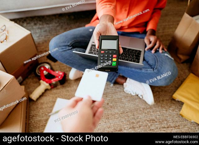 Young businesswoman with customer paying through credit card at home office