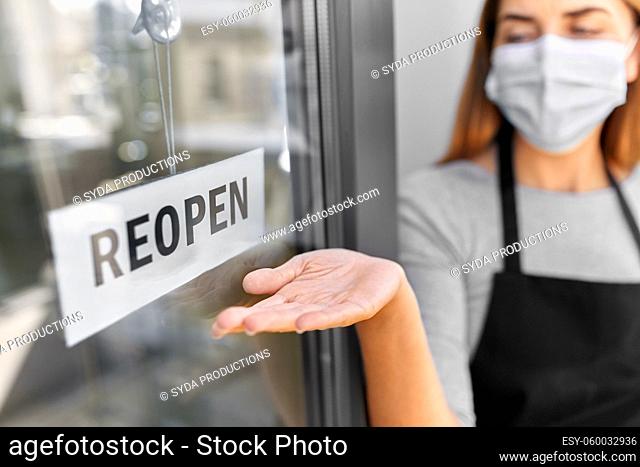 woman in mask showing reopen banner on door glass