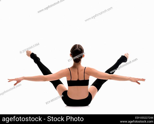 Slim girl in black sportswear streching gracefully isolated rearview on white background