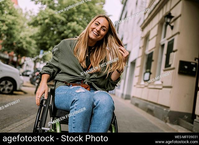 Happy woman sitting in wheelchair at sidewalk