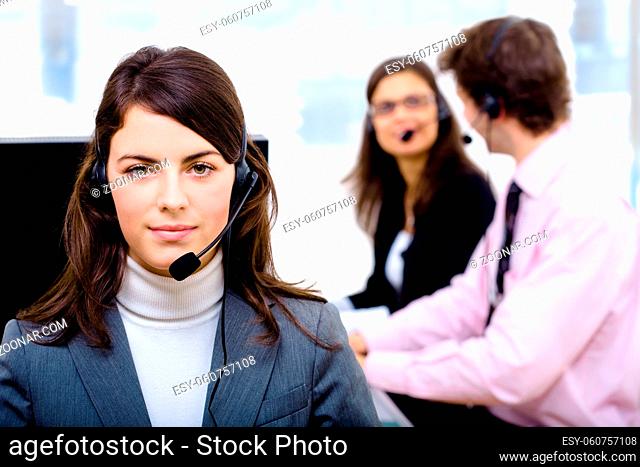 Customer service team working in headsets, smiling. Woman in front