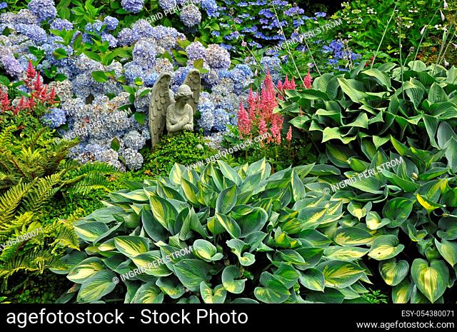 Decorative stone angel in colorful summer garden