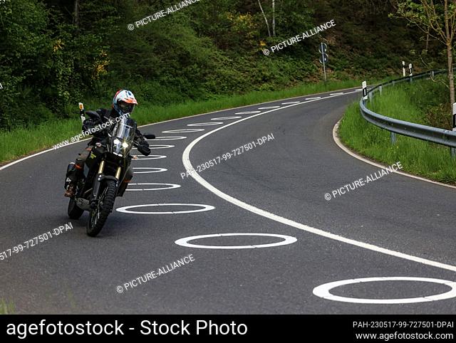 17 May 2023, North Rhine-Westphalia, Hürtgenwald: A motorcyclist rides through a switchback with circles painted on the roadway near Vossenack