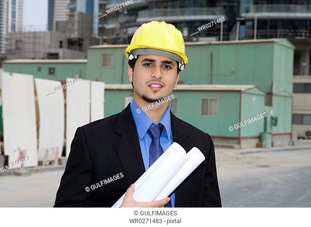 Businessman holding blueprints at construction site, smiling, portrait