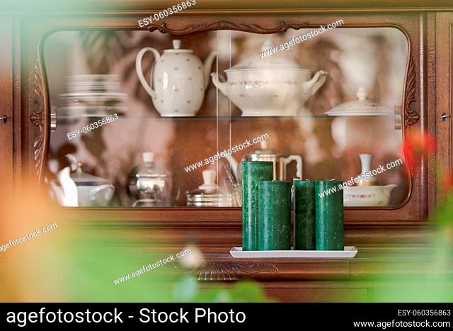 Front of wooden old sideboard filled with grandmother's teapots and plates seen through blurred foreground of room plants