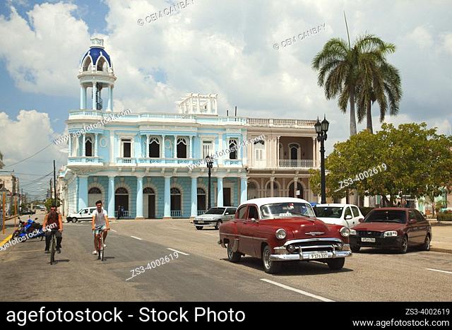 Cyclists and an American car in front of the colonial buildings at Parque Jose Marti with Palacio Ferrer at the background, Cienfuegos, Cienfuegos Province
