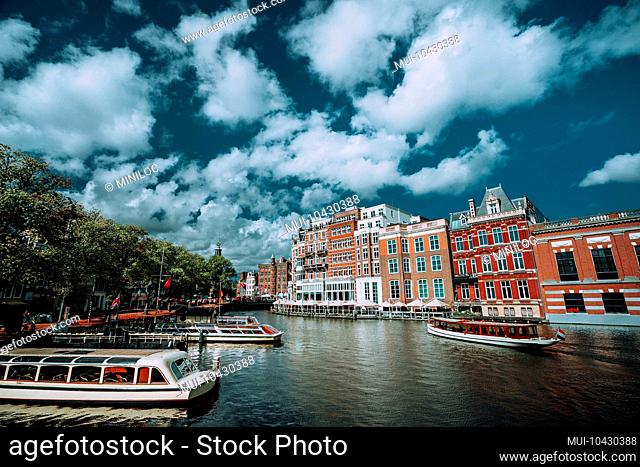 Classical Amsterdam cityscape. Cruise boats floating on the channel, river side promenade, cafes, typical Dutch architecture