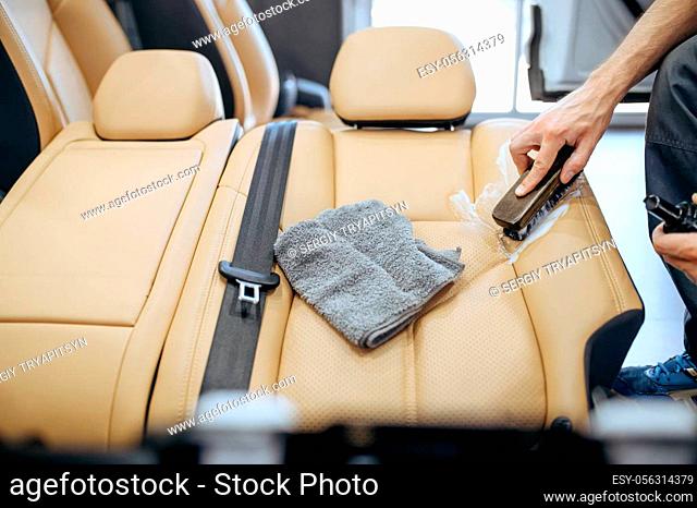 Worker with brush and spray wipes removed car seat, top view, dry cleaning and detailing. Vehicle washing in garage, thoroughly care of automobile