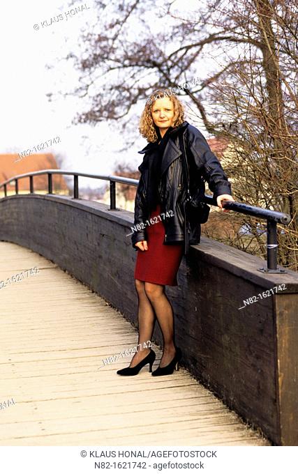 Well-dressed woman standing on wooden footbridge over a river and looks in the camera - Bavaria/Germany
