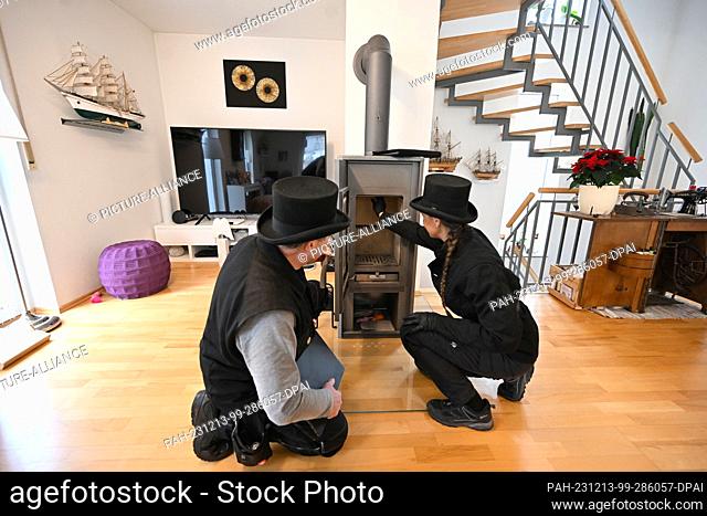 PRODUCTION - 13 December 2023, Bavaria, Munich: Chimney sweep Udo Löbel (l) and his daughter Diane Löbel inspect a wood-burning stove (single room fireplace for...