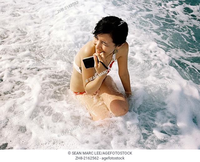 A young woman with her camera sits in foamy water on the beaches of Chi Shing Tan in Hualien, Taiwan