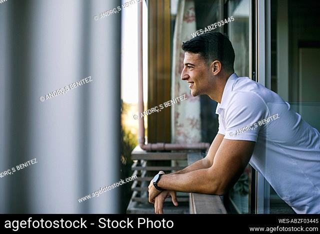 Smiling man looking away while leaning on balcony railing
