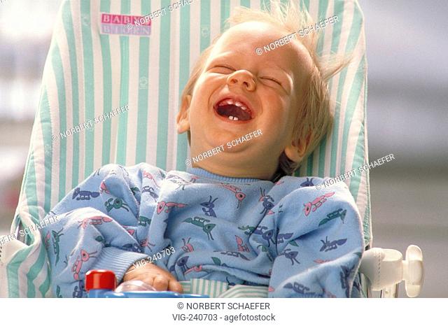 portrait, baby, 6 months, sits in a pyjama in a baby-seesaw laughing loud showing his 5 milkteeth  - 0, GERMANY, 08/10/2002