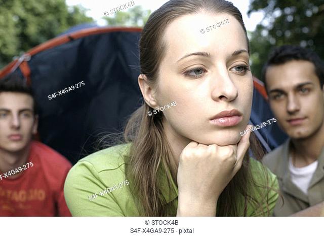 A young contemplative woman and two men in front of a tent in the background
