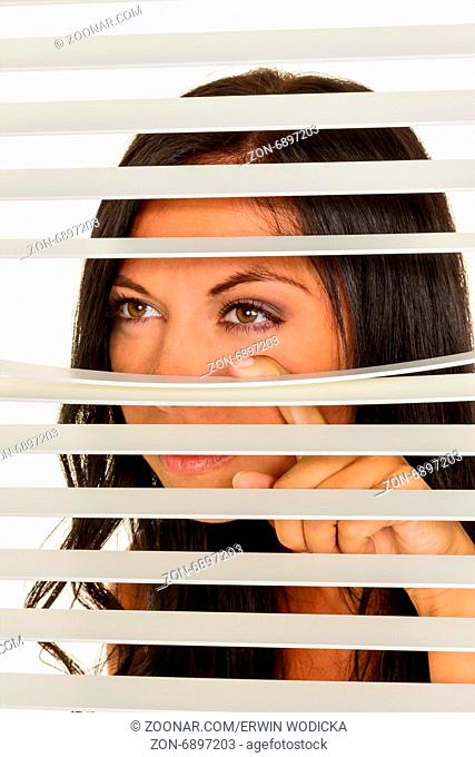 Eine junge Frau beobachtet etwas durch die Jalousie ihres Fensters