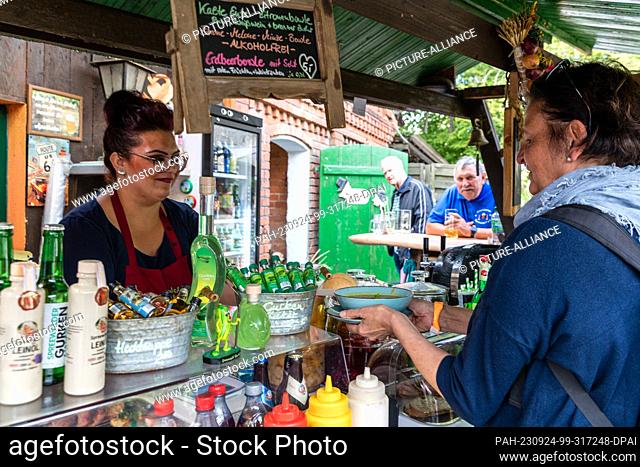24 September 2023, Brandenburg, Lübbenau/Ot Lehde: At a sales booth in the Spreewald village of Lehde, a saleswoman hands a plate of pumpkin soup to a customer