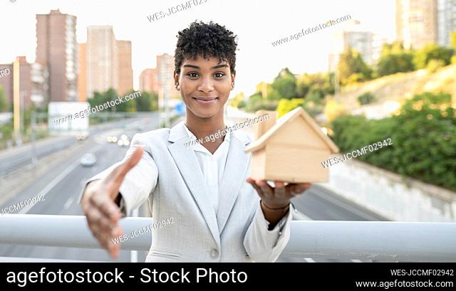 Saleswoman holding home model while greeting with handshake on bridge