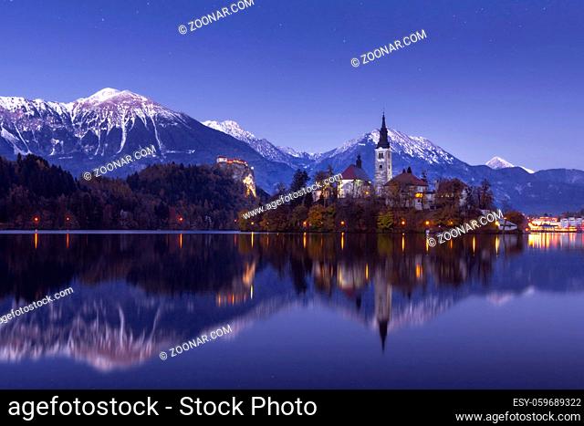 Scenic view of lake Bled at winter night with castle rock and St Martin church under beautiful starry sky reflected in lake water