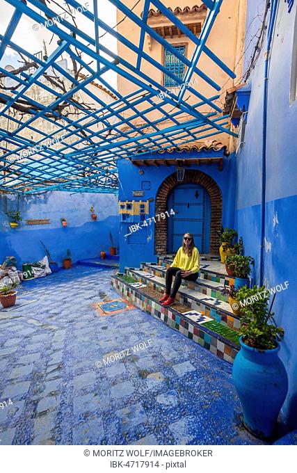 Young woman in the old town sits on a staircase, blue house walls, medina of Chefchaouen, Chaouen, Tangier-Tétouan, Kingdom of Morocco