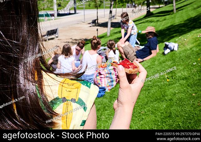 15 May 2022, Brandenburg, Potsdam: A girl eats a jam sandwich as families picnic in Potsdam's Volkspark. Photo: Annette Riedl/dpa