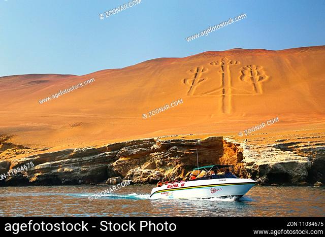 Tourist group in a boat near Candelabra of the Andes in Pisco Bay, Peru. Candelabra is a well-known prehistoric geoglyph found on the northern face of the...