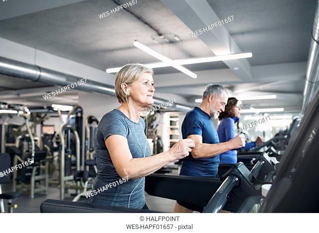 Group of fit seniors on treadmills working out in gym, man smiling