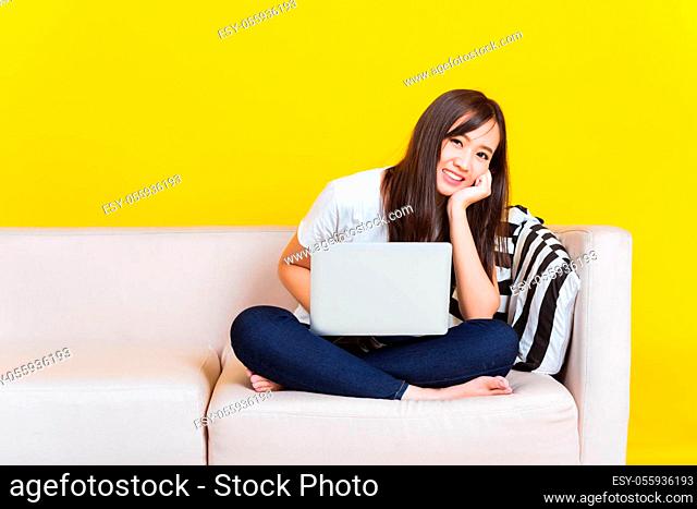 Portrait Asian of happy beautiful young woman work from home she sitting on sofa using laptop computer in house living room studio shot isolated on yellow...