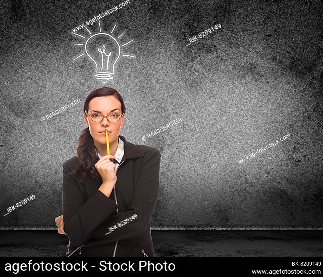 Light bulb drawn above head of young adult woman with pencil in front of wall with copy space