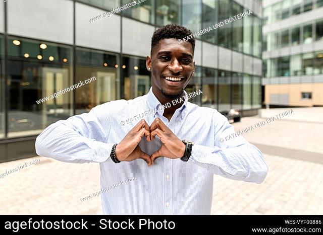Smiling man gesturing heart shape on footpath