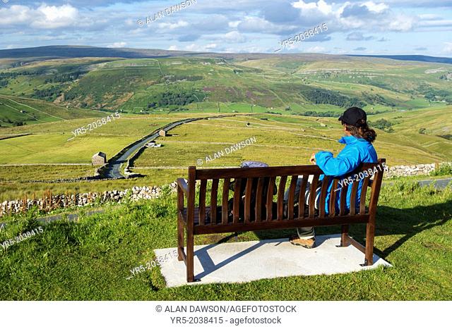 Female hiker on seat overlooking Buttertubs pass in The Yorkshire Dales National Park. Yorkshire, England, UK. View over Buttertubs pass