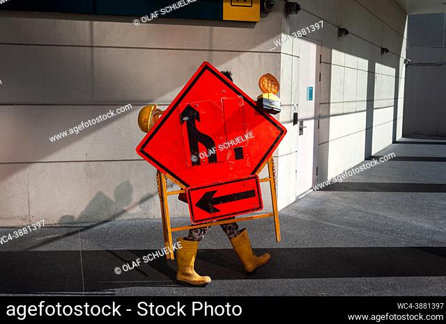 Singapore, Republic of Singapore, Asia - A worker carries equipment with street signs and warning lights in the city centre during the lasting corona crisis
