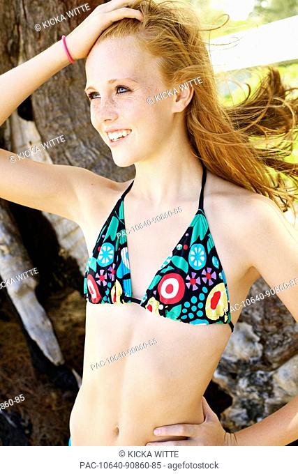 Teenage girl with freckles and red hair models her bathing suit outside