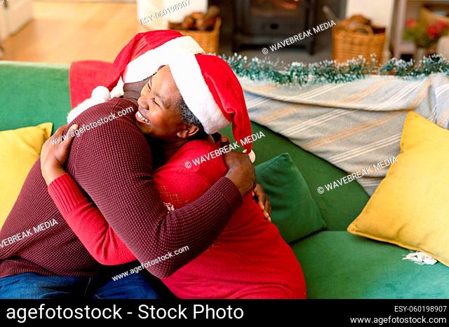 Happy african american senior couple hugging on sofa at christmas time