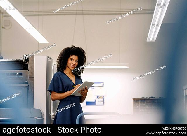 Smiling Afro female entrepreneur looking away while working on digital tablet at industry
