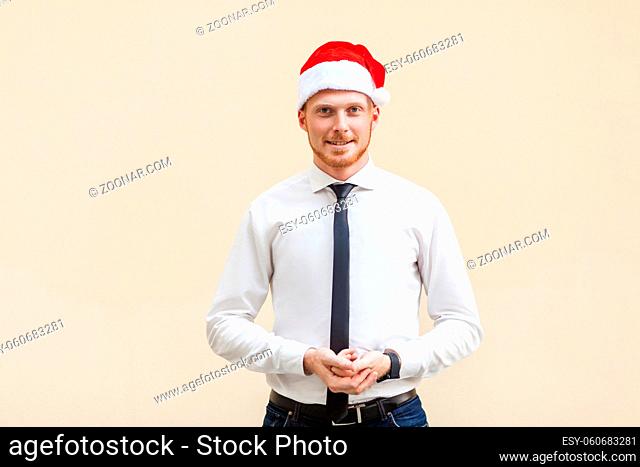 Young adult success ginger businessman looking at camera and smiling. Studio shot, light orange background