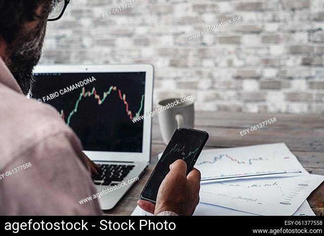 Stock and forex market business exchange with crypto currency business lifestyle. Back view of a man buying and selling stocks using laptop and mobile phone app...