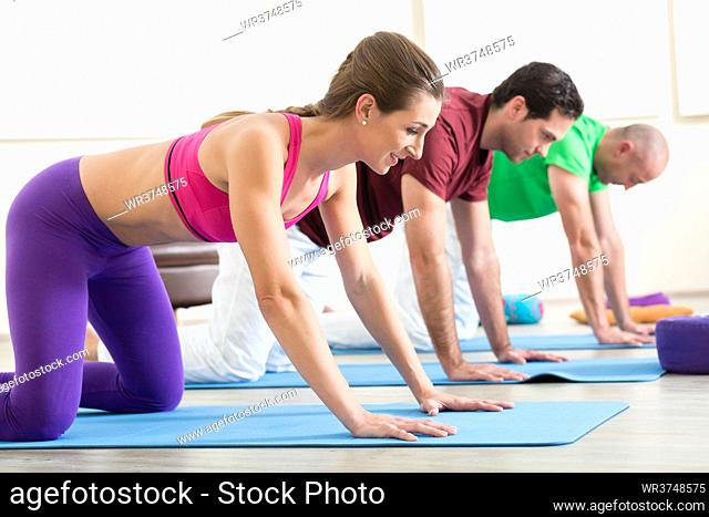 Young woman practicing yoga pose with two men on exercise mat