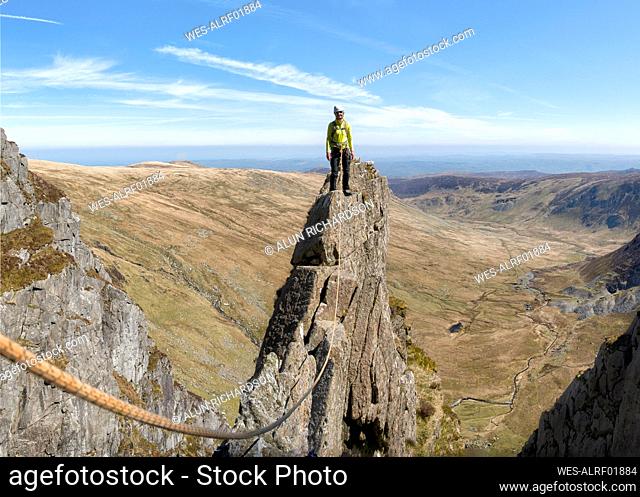 Senior woman standing on top of rocky mountain peak with climbing rope
