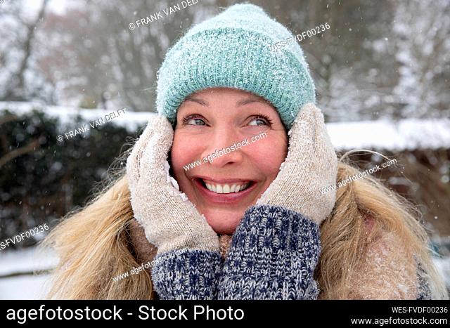 Happy blond woman standing with hand on chin at backyard during winter