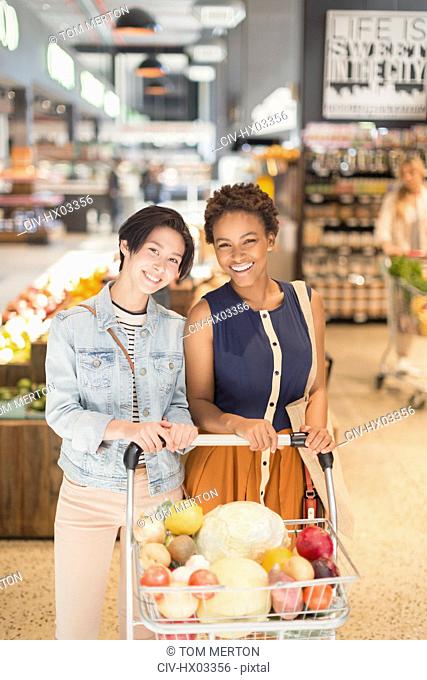 Portrait smiling young lesbian couple with shopping cart grocery shopping in market