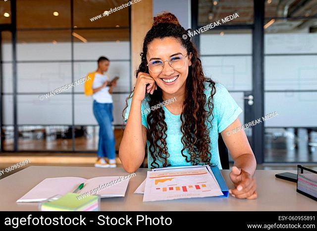 Portrait of smiling young businesswoman in casual sitting with charts at desk in creative office