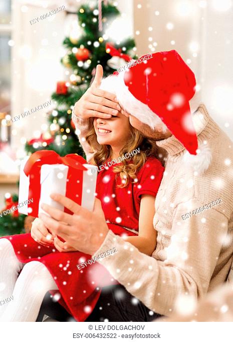 christmas, holidays, family and people concept - smiling father and daughter in santa hats holding gift box and covering eyes at home