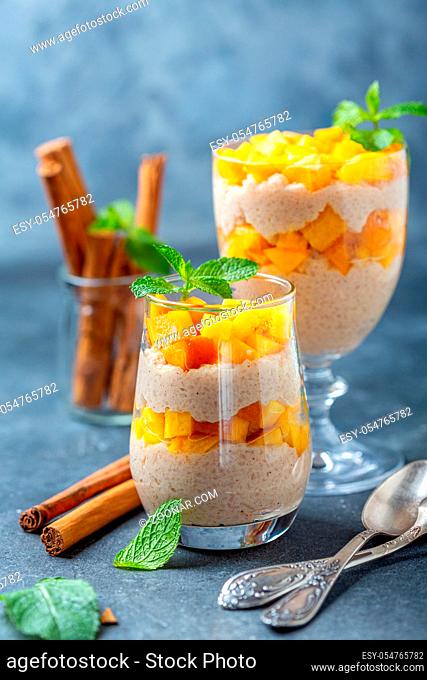 Rice pudding with peach slices and spices in glasses on a textured gray background, selective focus