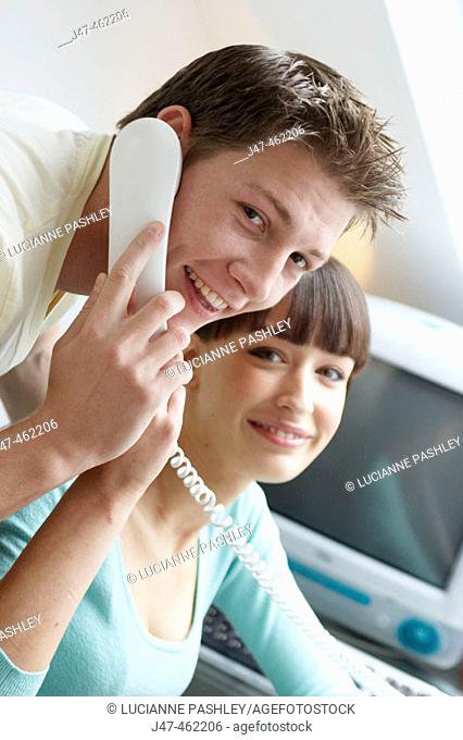 young couple sitting together in the office hes on the phone both smiling to camera