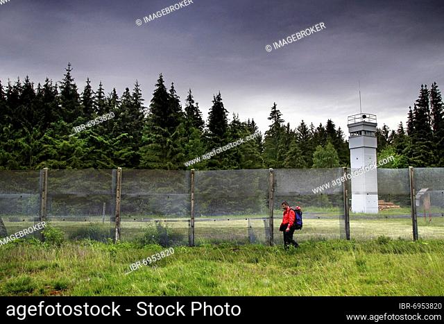 Hiker, man with backpack at former German-German border, border barrier with observation tower of the border troops of the GDR, border watchtower, border fence