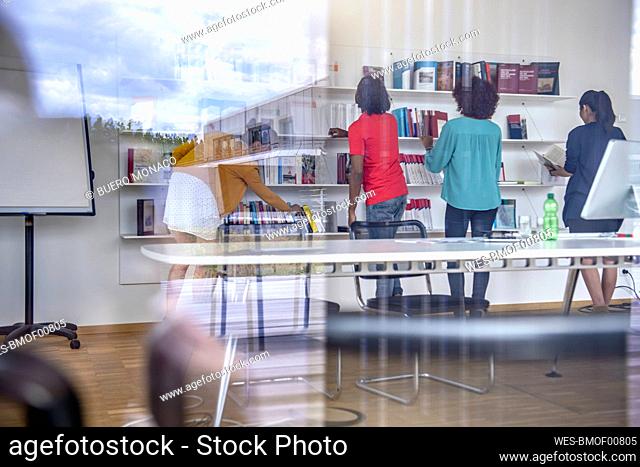 Male and female students standing near shelf while choosing books