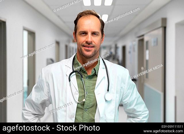 Portrait of smiling caucasian male doctor standing in hospital corridor